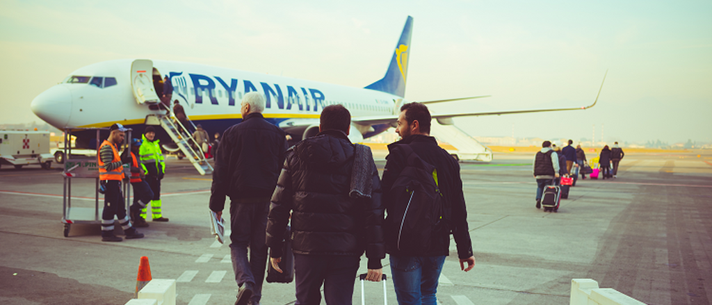 Back view of people carrying luggage boarding on a Ryanair plane